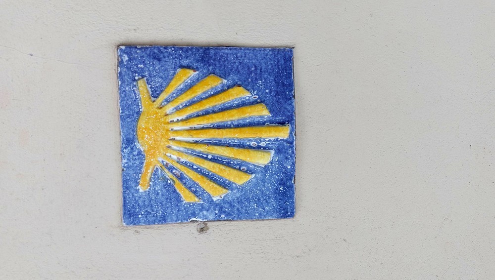 Gelbe Jakobsmuschel auf Hausmauer als Wegweiser für den Jakobs-Pilgerweg am 'Camino del Norte' bei Llanes