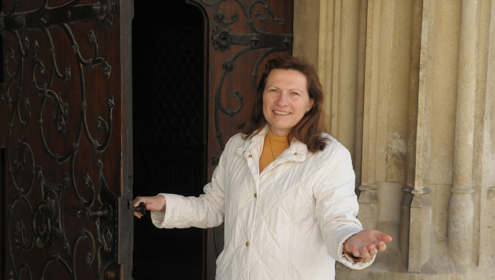 Elisabeth Obermayer, Pastoralassistentin, einladend vor der offenen Kirchent