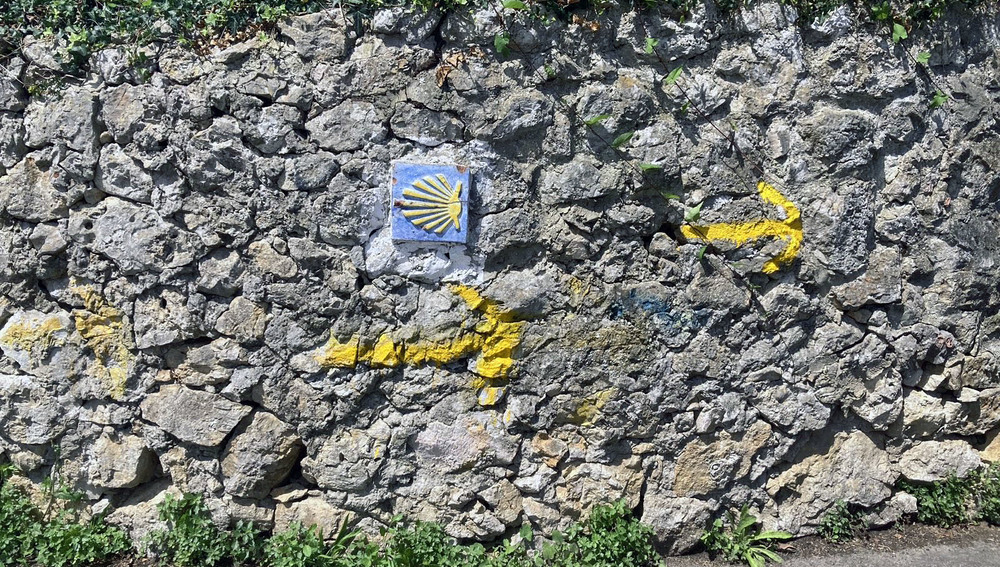 Gelbe Jakobsmuschel auf Steinmauer als Wegweiser für den Jakobs-Pilgerweg am 'Camino del Norte' bei Llanes